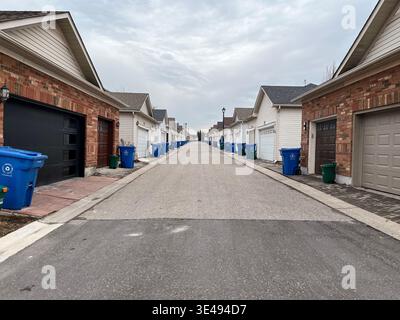 March 26, 2026 - Aurora, Ontario, Canada: Garbage day scene with extra large blue recycling bins and green organic waste bins lined up behind garages Stock Photo