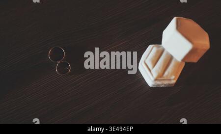 Two gold wedding rings and a hexagonal velvet box on a dark wooden background Stock Photo