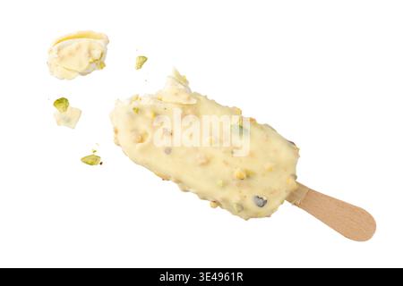 Ice cream covered White chocolate and crushed pistachio nuts on wooden stick flying on white background. Chocolate nuts sweet bitten popsicle is froze Stock Photo