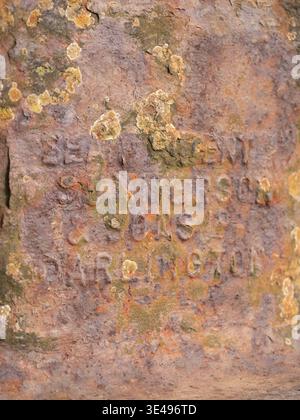 Close-up of embossed text on a rusty metal surface, with patches of lichen. Stock Photo