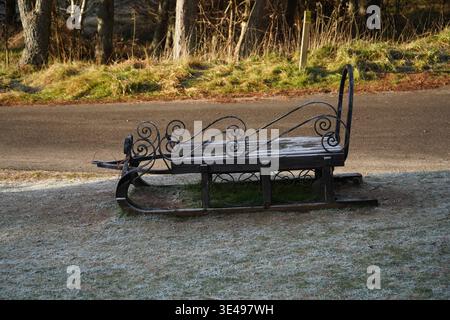 Empty Vintage Wrought Iron Sleigh on a Frosty Grass Verge Beside a Road in Winter Stock Photo