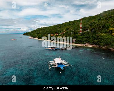 Aerial view of boats floating on turquoise waters meeting a lush coastline, watched over by a red and white tower, Oslob, Cebu, Philippines. Stock Photo