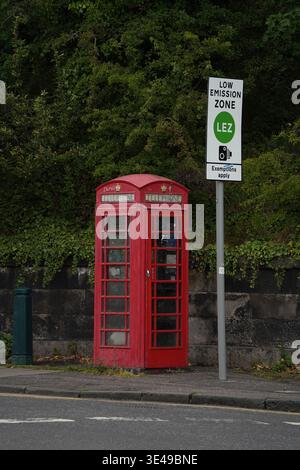 A classic British red K6 telephone kiosk standing next to a modern Low Emission Zone (LEZ) entry sign at a city boundary in Edinburgh, Scotland. Stock Photo