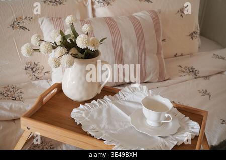Charming Cozy Bedside Arrangement with Floral Decor and Elegant Tea Set on Wooden Tray Stock Photo