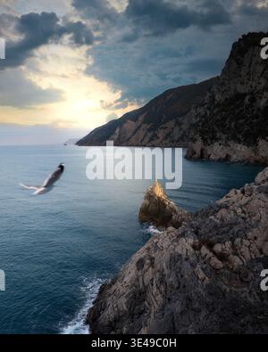 View of the rugged coastal cliffs and a seagull in flight over the blue sea under a dramatic cloudy sky in Porto Venere, Liguria, Italy. Stock Photo