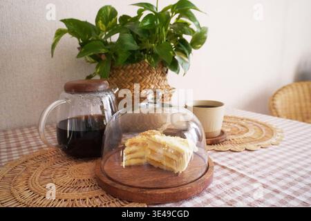 Delicious Layered Cake Under Glass Dome with Coffee and Potted Plant on Rustic Table Setting Stock Photo