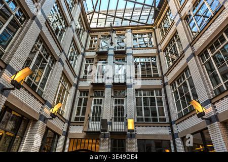 The inner courtyard of an Art Nouveau exhibition complex: a multi-storey atrium with white tiled walls, a glass roof and wall sconces; typical architecture of Leipzig’s exhibition arcade system. Leipzig, Saxony, Germany Stock Photo