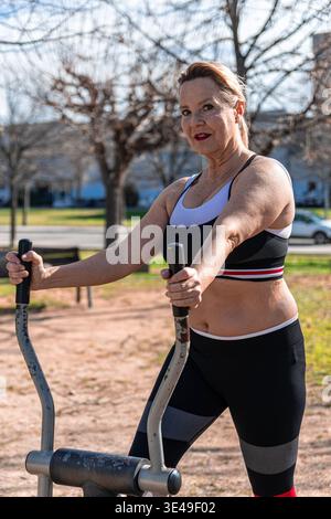 Senior woman exercising on an outdoor fitness machine in a public park, focusing on health and an active lifestyle, embodying wellness and vitality du Stock Photo