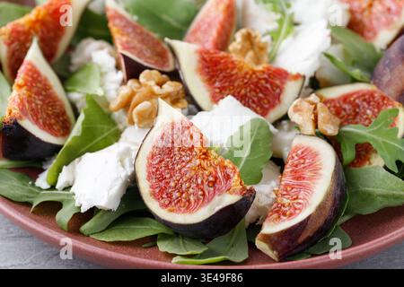 Tasty salad with sliced figs, crushed soft goat cheese, walnut and fresh arugula leaves on red plate closeup. Stock Photo