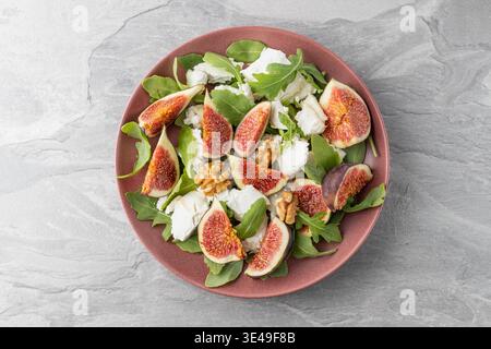 Tasty salad with sliced figs, crushed soft goat cheese, walnut and fresh arugula leaves on red plate grey slate background. Healthy food Stock Photo