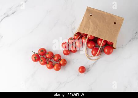 Small paper packaging of red cherry tomatoes on marble table background. Brown craft paper bag with handles and holes for organic vegetables in superm Stock Photo