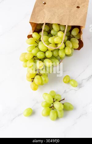 Fresh harvesting seedless green yellow grape bunch falling from paper bag on marble table background. Stock Photo