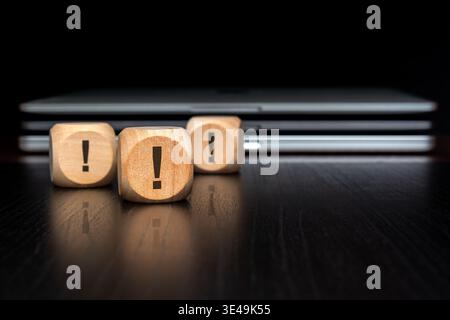 Exclamation mark wooden blocks with blurred laptop stack. Warning, attention, cybersecurity alert and urgent IT notification concept. Stock Photo