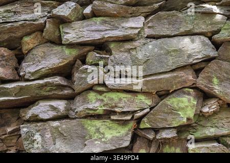 Rugged dry stone wall showcasing natural rock texture and green moss Stock Photo