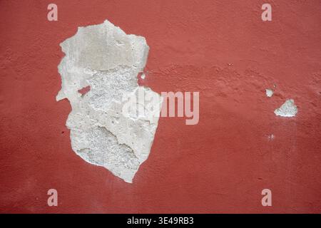 Red stucco wall showing peeling paint, cracking, and decay, creating an abstract background texture Stock Photo