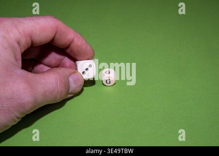 Hand holding a white dice, another on a green background Stock Photo