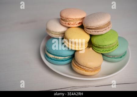 close-up of a stacked assortment of pastel macarons on a white plate, soft natural light revealing delicate shells and creamy fillings, set on a pale Stock Photo