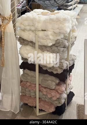 a tall stack of soft textured blankets in various colors on a retail display stand. Stock Photo