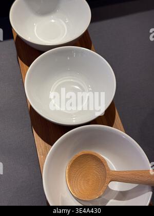 three empty white ceramic bowls on a wooden serving board with a spoon, clean kitchen concept Stock Photo