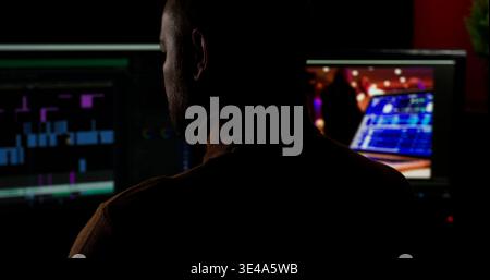 Person works on video editing in a dark room with computer screens showing editing software and footage in the background Stock Photo