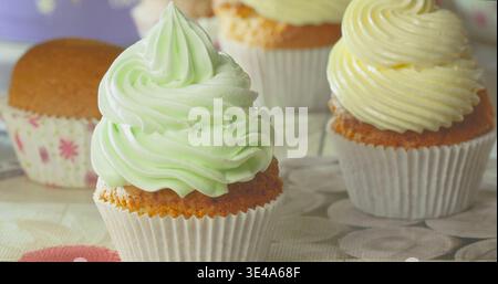 Cupcakes with colorful frosting are placed on a table in a bright setting during a casual gathering Stock Photo