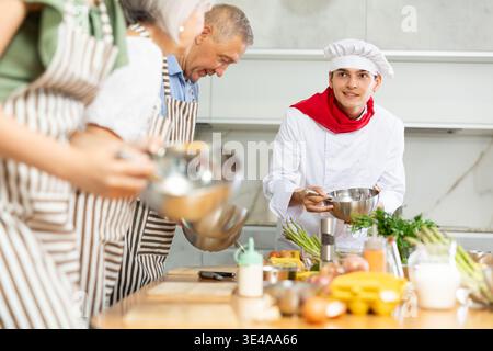 Positive young man chef of cooking course teaching attendees how to mix sauce Stock Photo