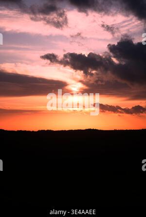 Pink and Orange Cloudy Sunset Over Silhouetted Horizon Stock Photo