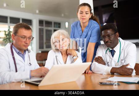 Doctors sitting around the table looking at the notebook Stock Photo