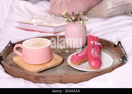 Aromatic coffee in cup, eclairs, and beautiful flowers on bed, closeup Stock Photo