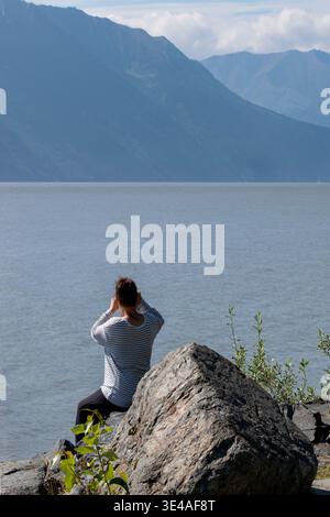 Anchorage, Alaska.  A woman scans the water with her binoculars looking for whales on Beluga Point, a rocky outpost jutting into the waters of Turnaga Stock Photo