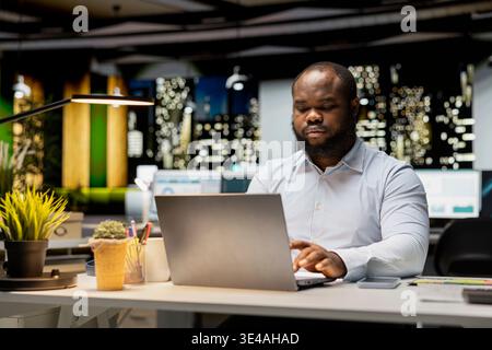 African american worker proofreading a document before transcribing on notebook, extracting the main ideas from reports on laptop. Expert documenting after hours late at night. Stock Photo