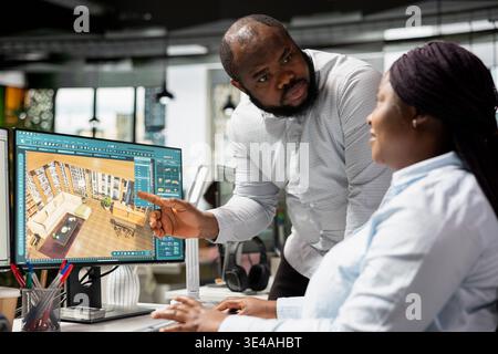 Black employees team using architectural CAD software for modern layout design, 3D rendering program on dual monitors. Architectural floor plan with tools and assets used for remodeling. Stock Photo