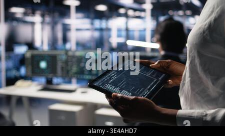 Close up of data center programmer using tablet, writing code for resource optimization, performing updates. Server room employee using device, compiling software patches to fix bugs, camera A Stock Photo