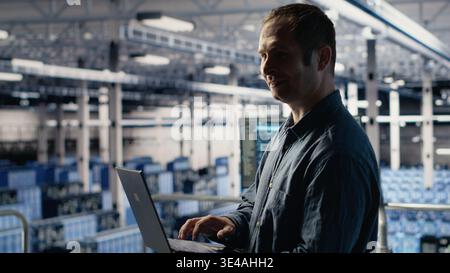 Data center technician monitors deep learning process with laptop, reviewing operational metrics. IT expert reviews neural networks reports during inspection to verify ongoing stability Stock Photo