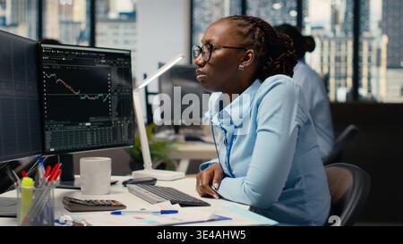 Portfolio manager in brokerage company office analyzes stock market trends to increase returns. African american woman tracks stock exchange metrics to identify investment opportunities Stock Photo