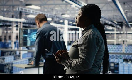 Teamworking data center programmers investigate neural networks configuration, making adjustments for optimal function. Server hub colleagues work together to check deep learning errors, camera B Stock Photo