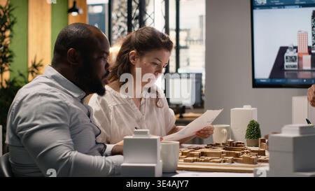 Team members work together in office with architectural software and 3D models to envision a successful residential property with smart city infrastructure goals. Urban development. Stock Photo