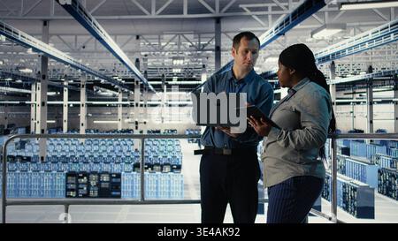 Server room coworkers scan infrastructure for security issues using laptop. Data center system administrators using notebook to organize file backups and plan recovery steps, camera A Stock Photo