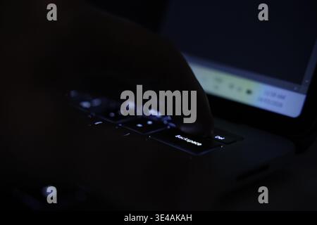 A finger about to push the delete or backspace undo button or tab on an illuminated computer keyboard in the dark. Stock Photo
