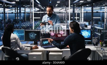 System administrators in data center struggle with computer bugs while using AI. Frustrated server farm coworkers doing brainstorming to fix system errors while using artificial intelligence, camera A Stock Photo