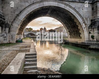 Clouds near sundown reflect on the water through the archway of a bridge on the Tiber River in Rome. Stock Photo