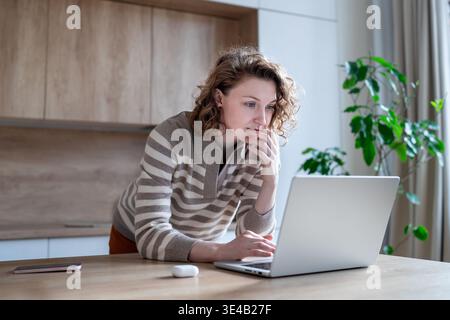 Serious concentrated young woman using laptop for remote work, research or online learning from home Stock Photo