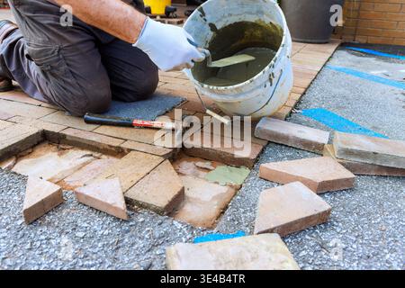 Worker kneels while pouring mortar into gap between bricks in pathway during pavement repair in yard. Stock Photo
