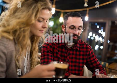 Casual coffee meeting conversation between two young adults in a cozy cafe setting with warm lighting and relaxed atmosphere, focusing on discussion Stock Photo