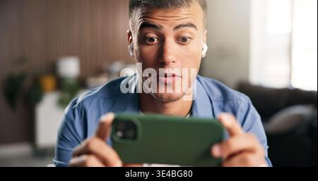 Earphones, surprise or man with smartphone in home, streaming web series or attention for online show. Movie subscription, tech or person with shock Stock Photo