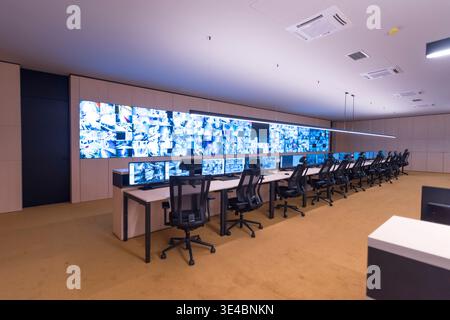 Modern security operations center with multiple workstations and large video wall displaying surveillance camera feeds. Concept of monitoring, safety, Stock Photo