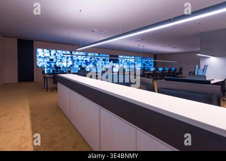 Modern security operations center with multiple workstations and large video wall displaying surveillance camera feeds. Concept of monitoring, safety, Stock Photo