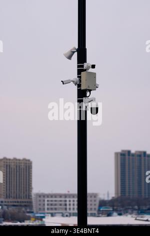 A tall pole with multiple security cameras overlooking an urban cityscape on an overcast day Stock Photo