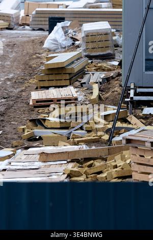 A cluttered construction site with scattered materials, insulation panels, and debris on muddy ground Stock Photo