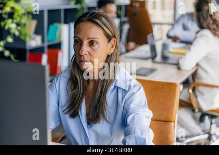 Dedicated Female Data Analyst Concentrating On Detailed Spreadsheet Analysis With Colleagues Working Nearby Stock Photo